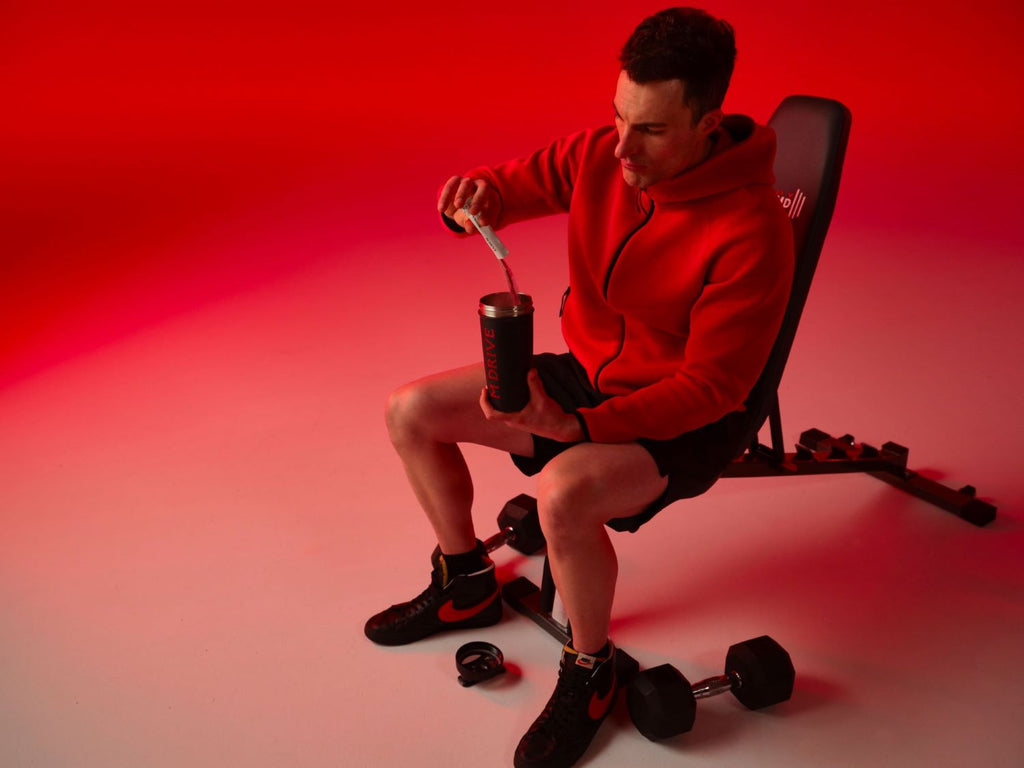 Man pouring pre-workout into shaker sitting on workout bench.