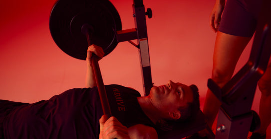 M Drive man bench pressing with a woman spotter