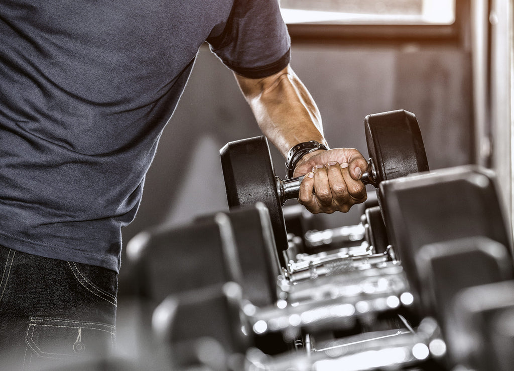 man lifting dumbbell off weight rack at gym