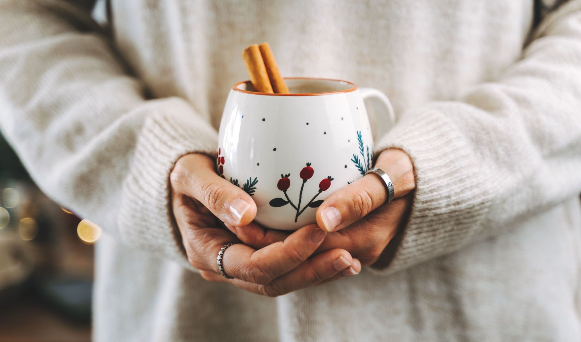 woman in cozy sweater holding mug of cocoa with cinnamon stick