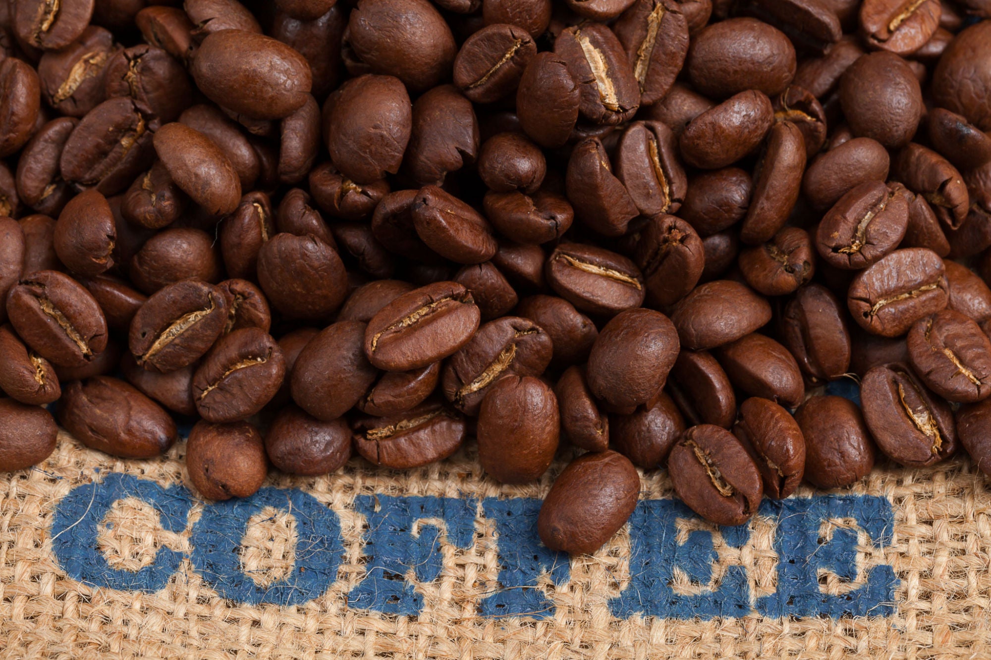roasted coffee beans on a canvas sack with the word coffee in blue