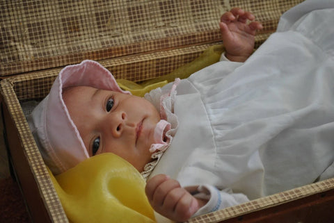 A baby girl wearing a white dress with a pink hat