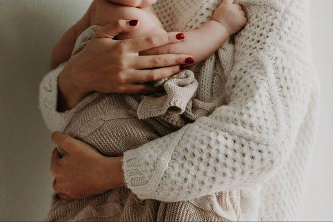 a women holding a baby wrapped in a beige blanket