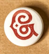 Image pf the button badge pin showing the Grimm & Co insignia in red on white.