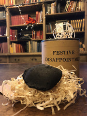 Festive Disappointment tin containing a briquette of charcoal and a sheet of jokes.