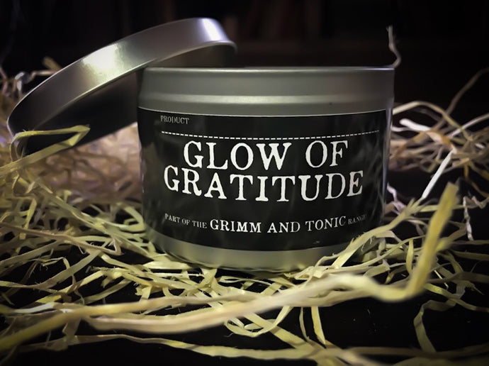 Image of Glow of Gratitude, a tinned candle with slip lid in the Grimm & Tonic range. Tin is silver with a black label and white text