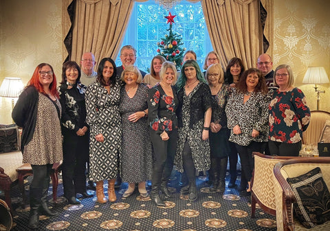 A group of 16 people, smartly dressed, in front of a Christmas tree, mainly looking happy