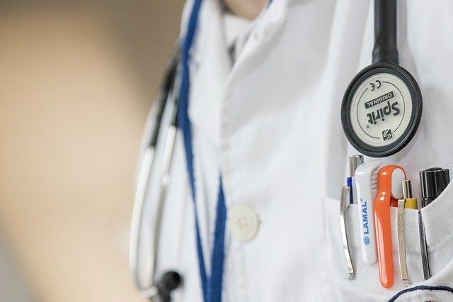 A doctor with a stethoscope around his neck and pens in his lab coat pocket