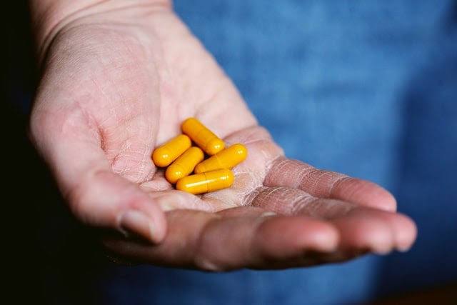 A man holding five orange capsules in the palm of his hand