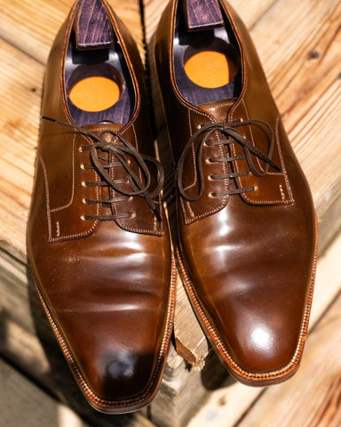 Top view of a pair of Color 4 shell cordovan Acme plain-toe derbies with purple shoe trees, on the corner of a wooden step