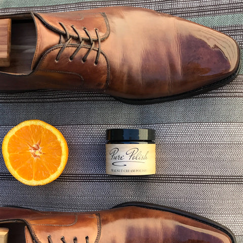 Orange slice next to a pair of polished leather derbies and a jar of Pure Polish
