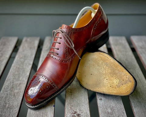 Vass Shoes Quarter Brogue Oxford men's dress shoes shined up with one on its side showing the sole, and the other on top facing diagonally.