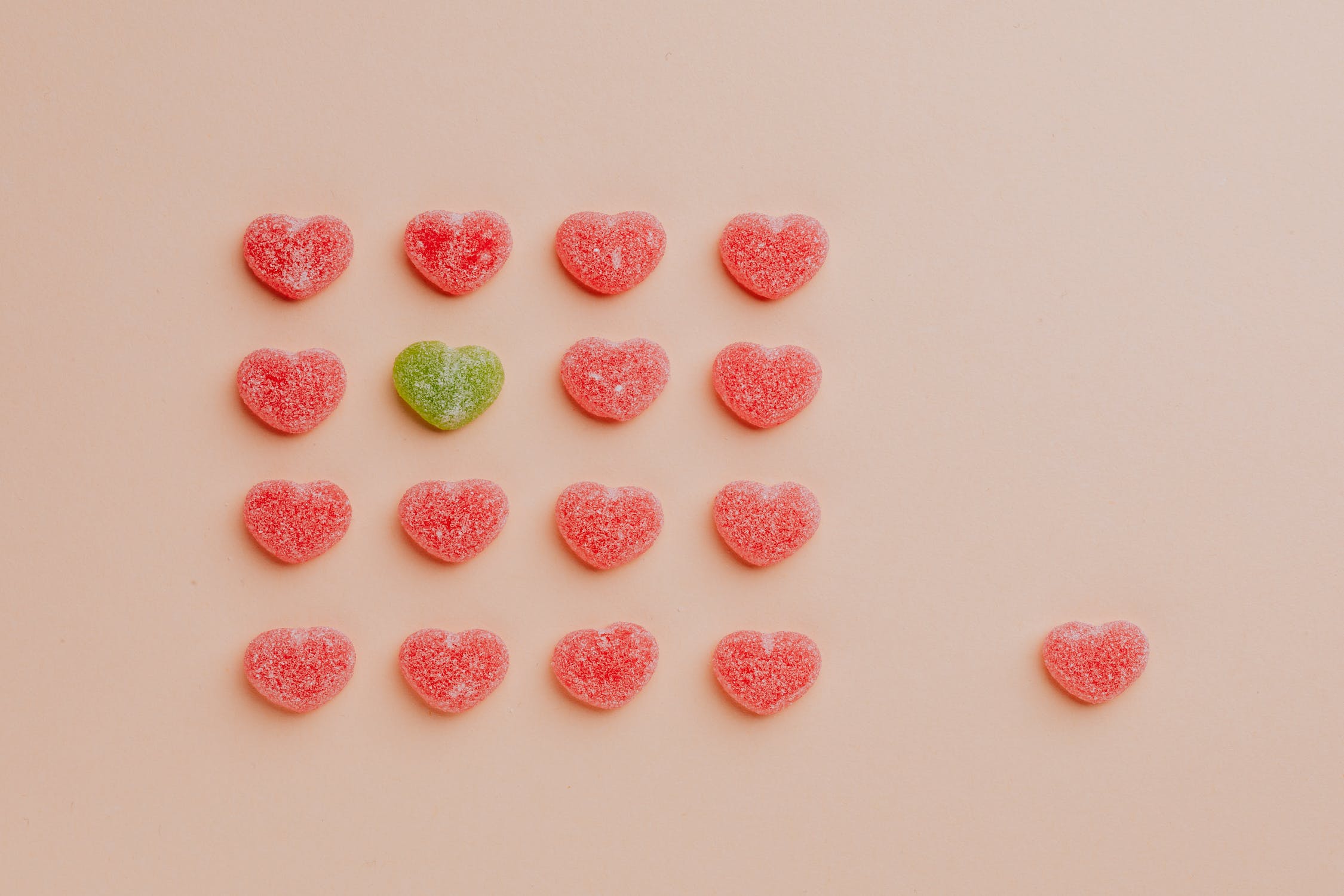 Caramelos gomosos en forma de corazón surtidos en filas con un caramelo a un lado sobre fondo rosa