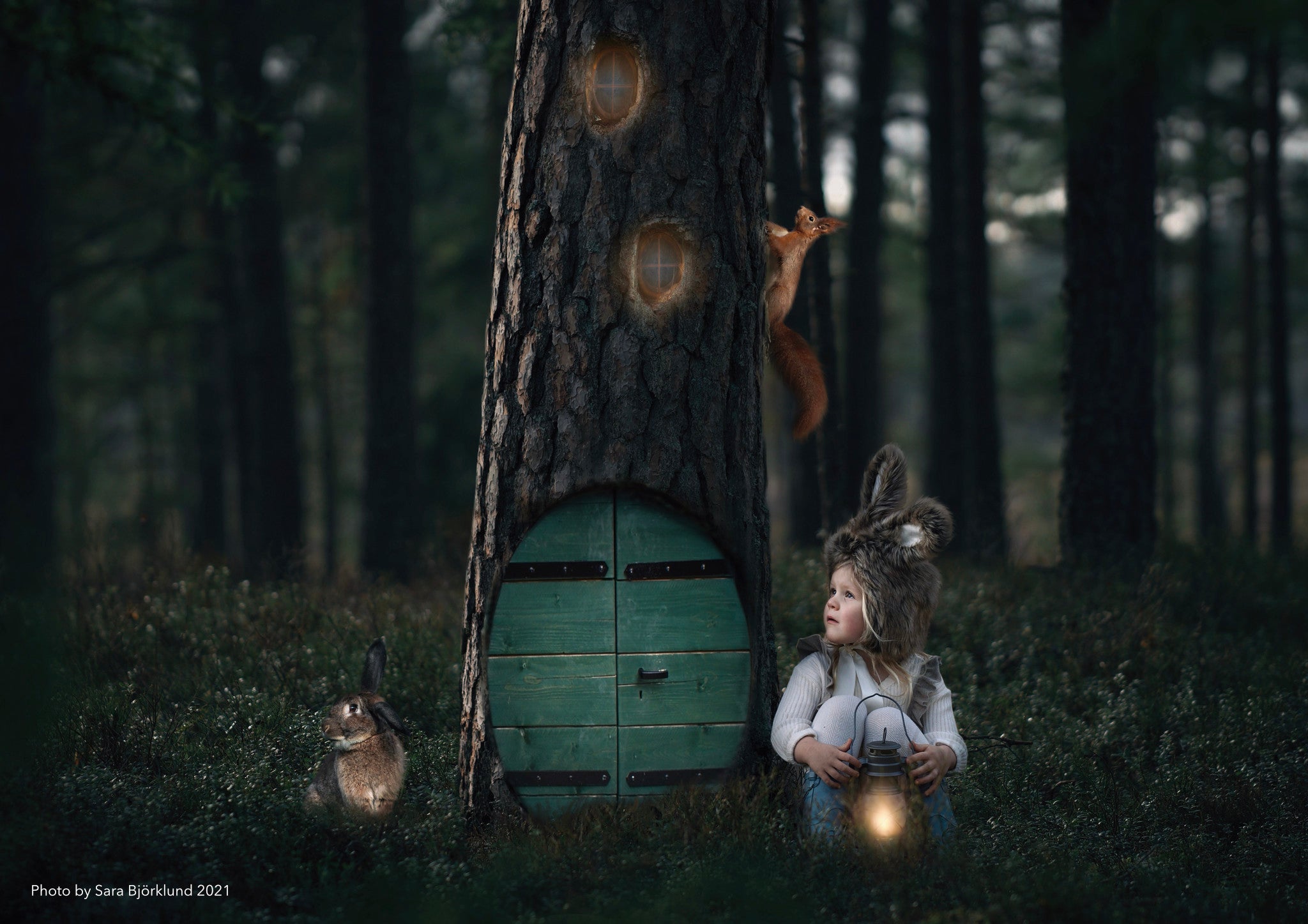 Small child with bunny ear hat sitting next to a big tree with a magic door.