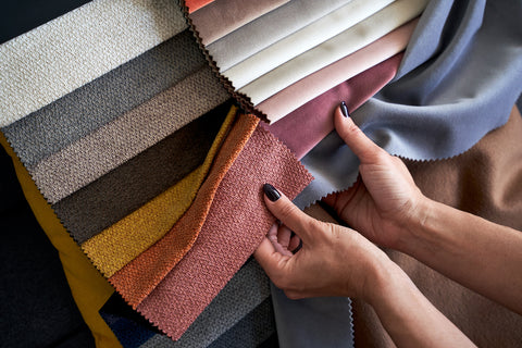 Choosing sustainable fabric color and texture from various colorful samples in a store. Female customer hands touching textile.