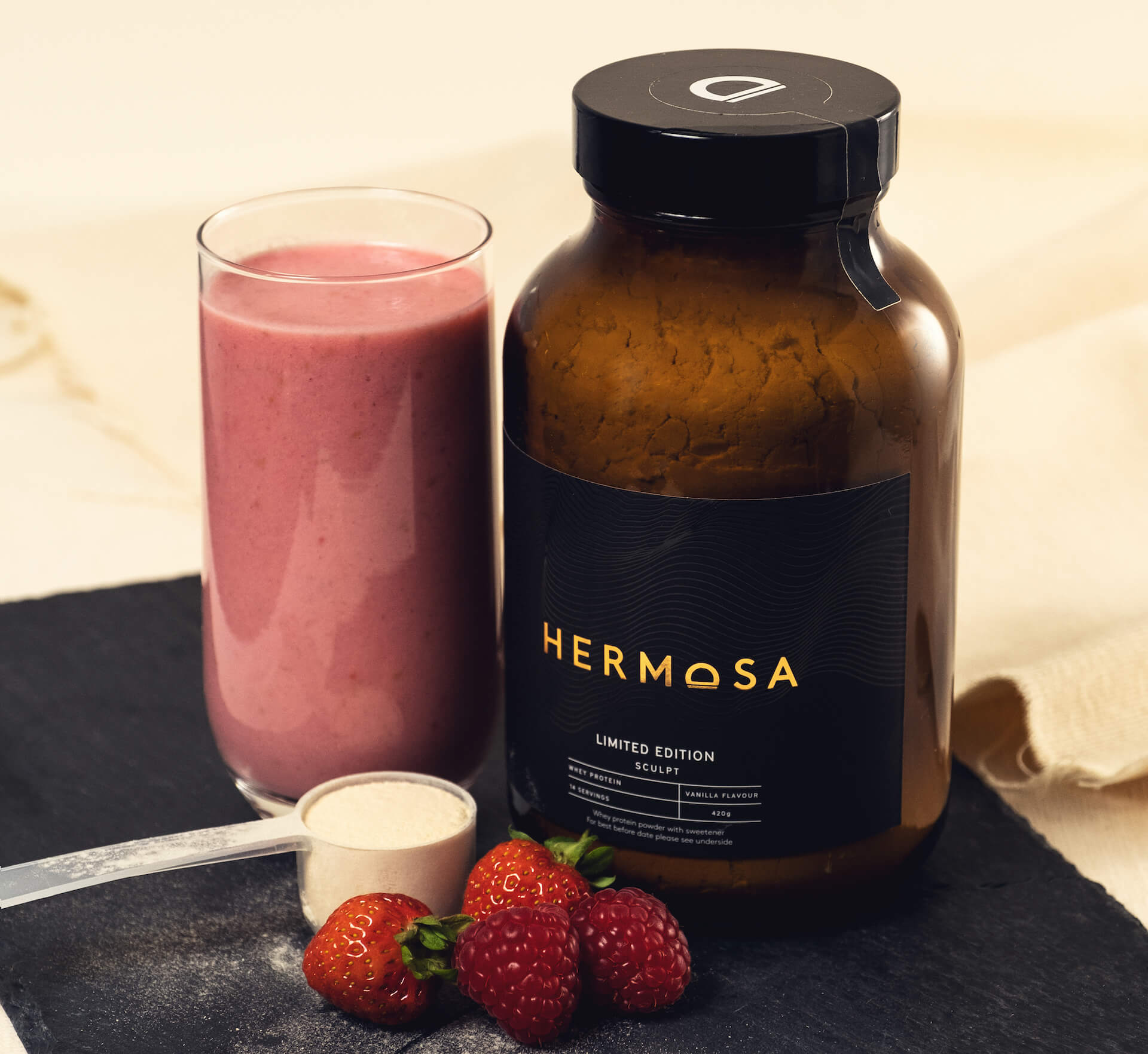 A berry protein smoothie next to a glass jar of HERMOSA protein powder.