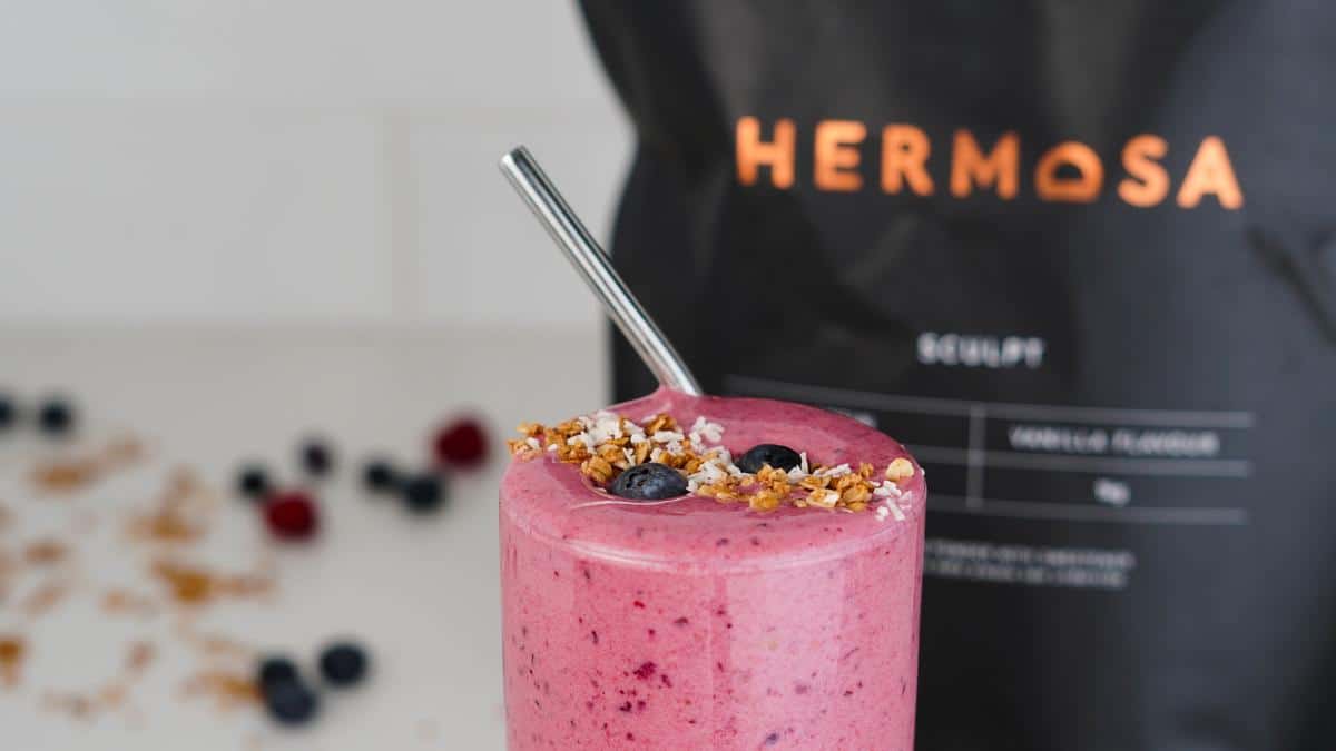 A berry smoothie with a bag of HERMOSA protein powder behind it.