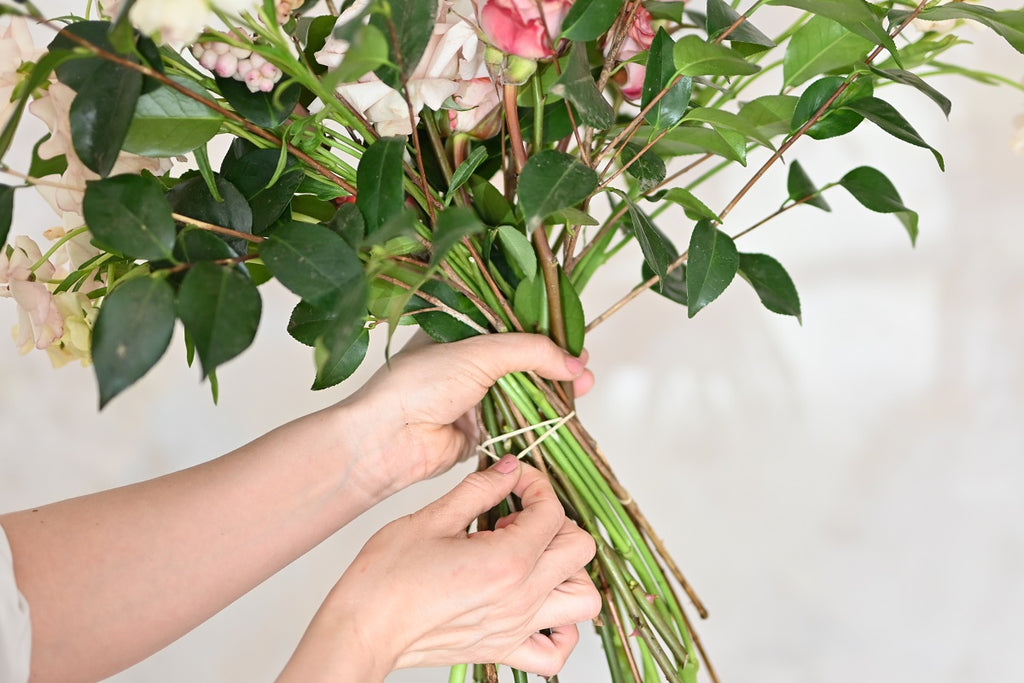 A woman binding a bouquet of flowers with a ribbon