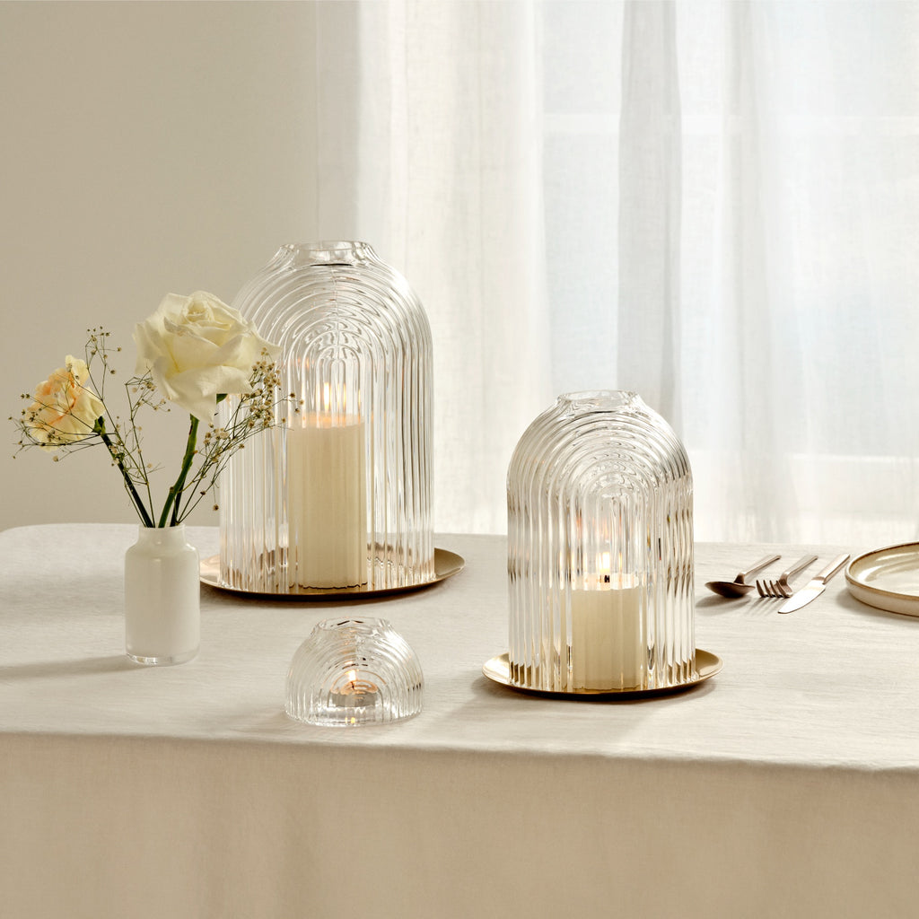 Rippled, clear leadfree glass domes on copper plates, functioning like candle holders in 2 sizes and a small votive holder. Presented on a table cloth with candles lit.