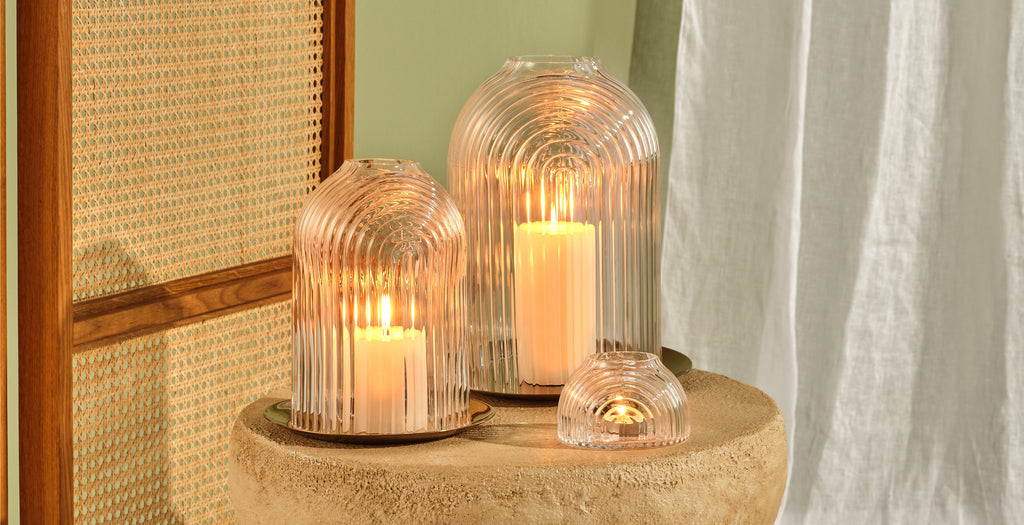 Rippled, clear leadfree glass domes on copper plates, functioning like candle holders in 2 sizes and a small votive holder. Presented on a marble table with candles lit.