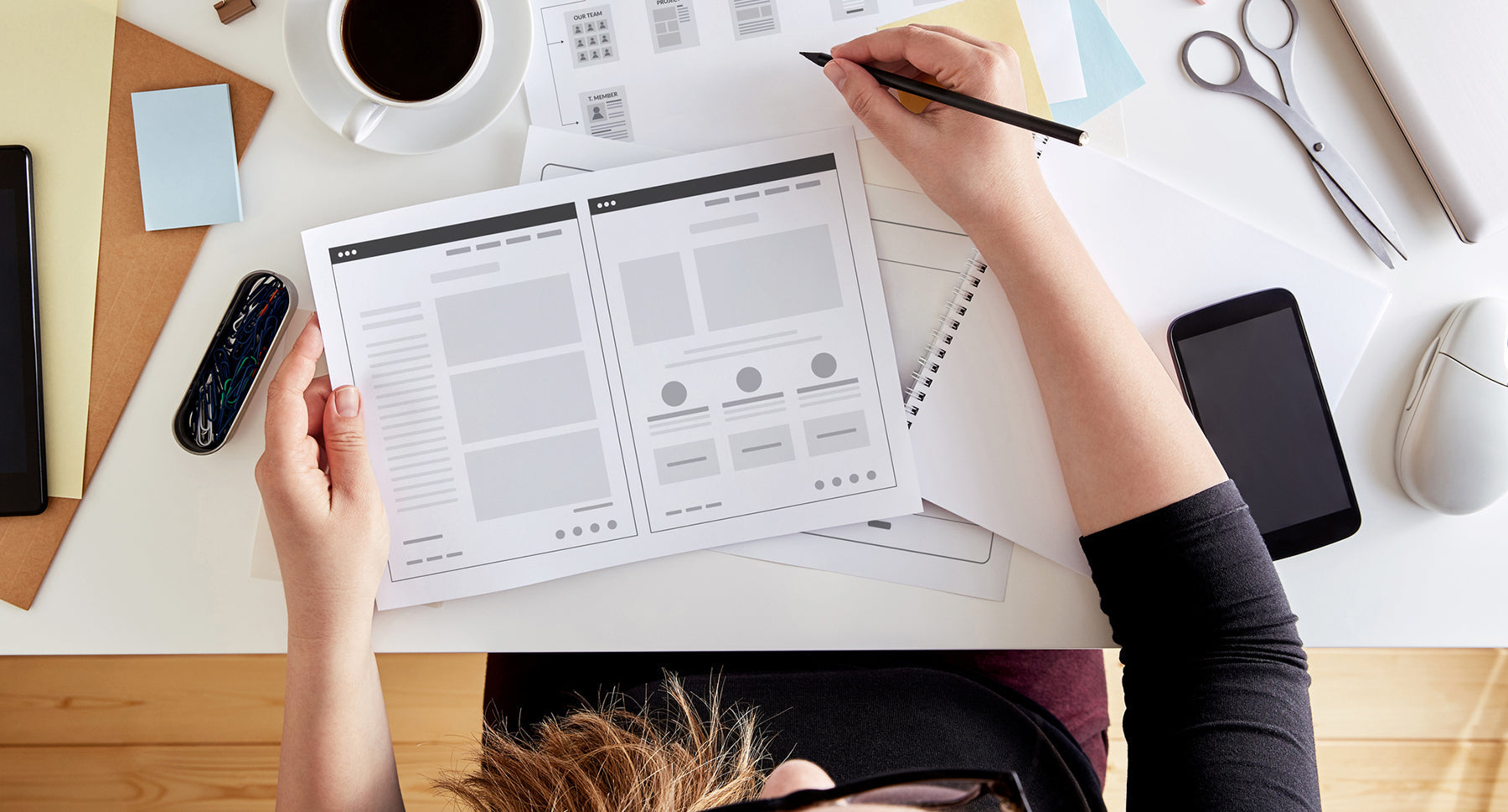 Photograph of a woman working on her website design with a sketch and prototype.