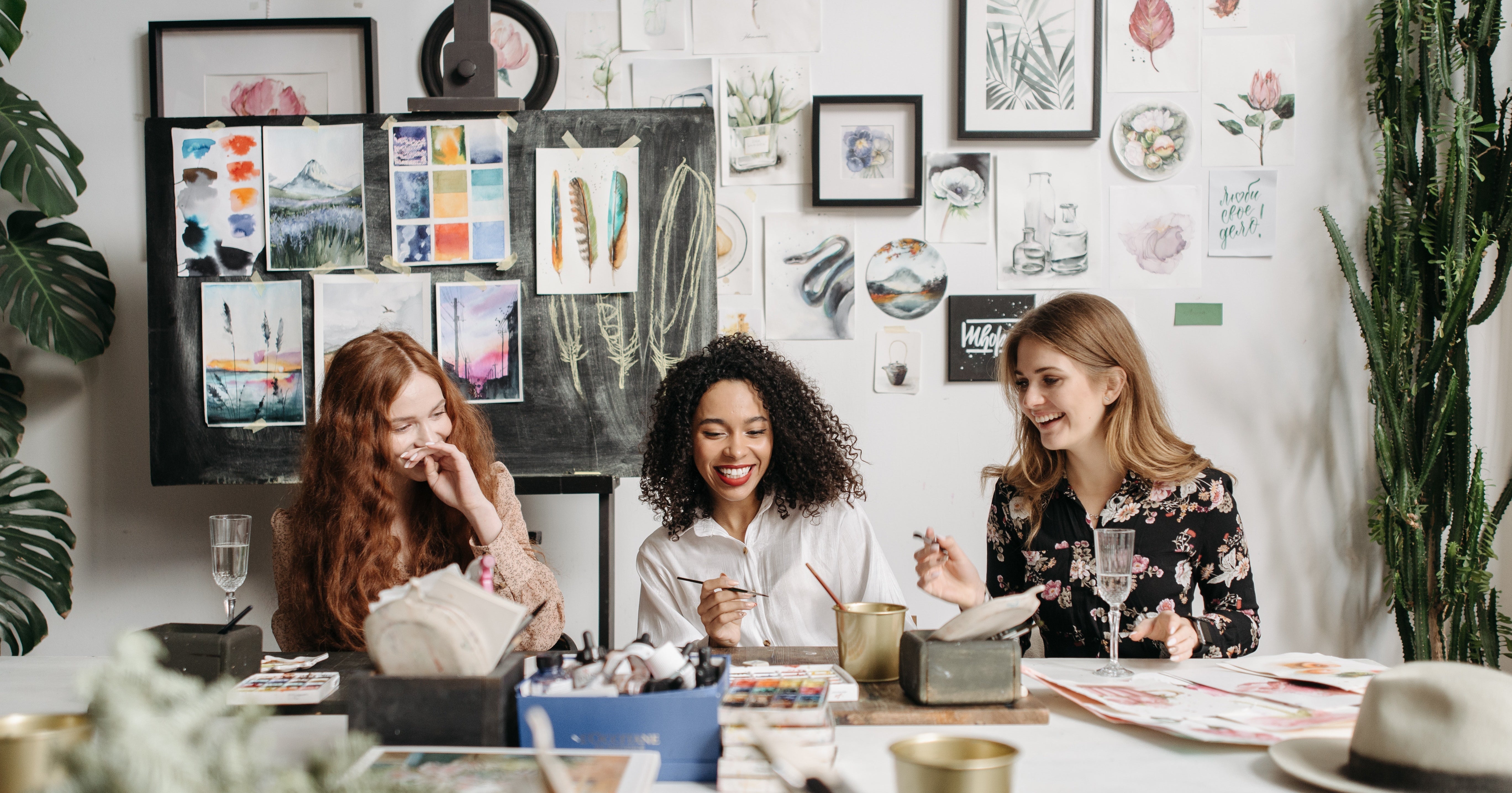 Three people sit in an art studio sharing a drink and a laugh