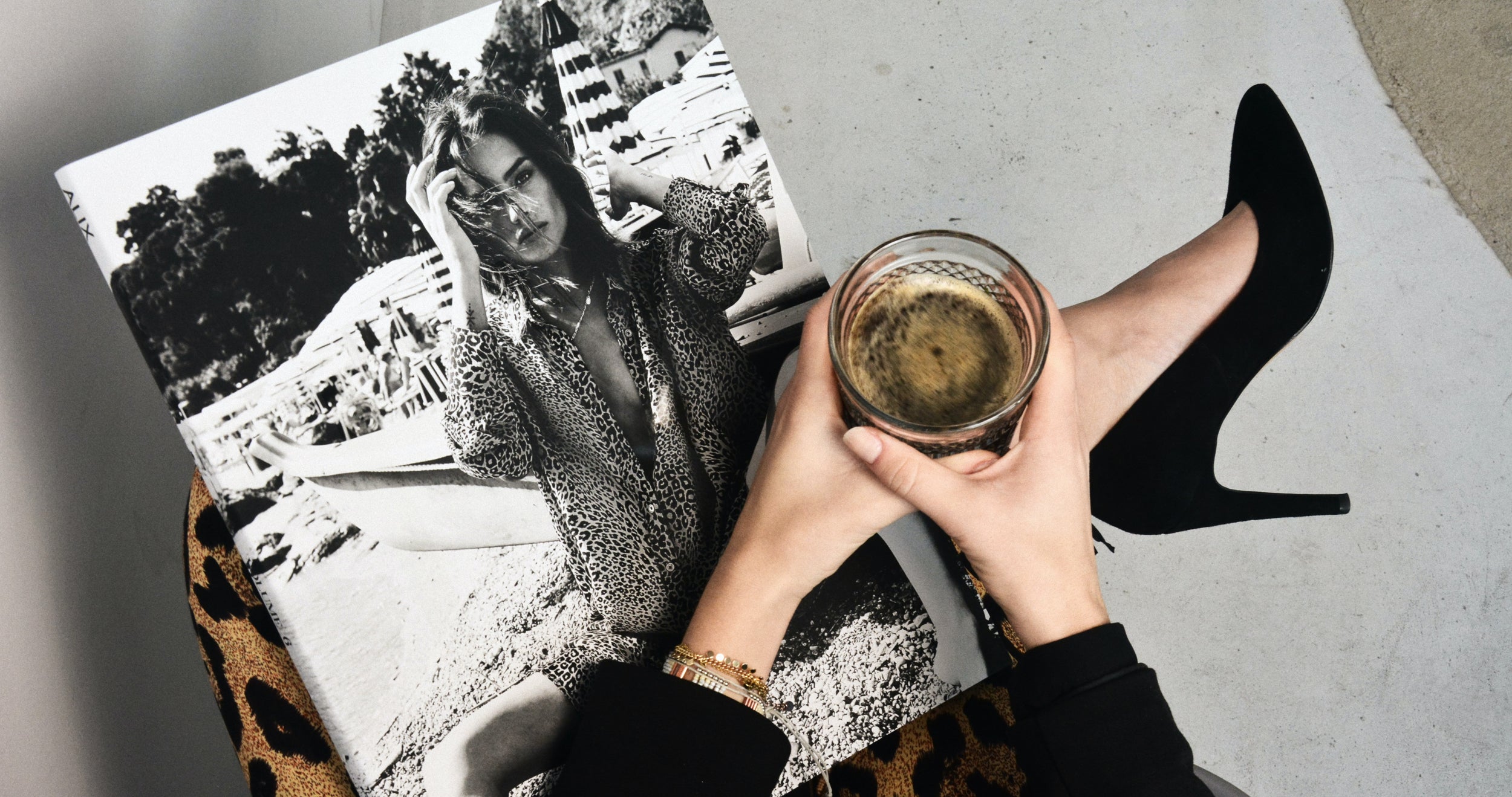 Person shot from above showing only the lap and hands holding a fashion magazine and a drink