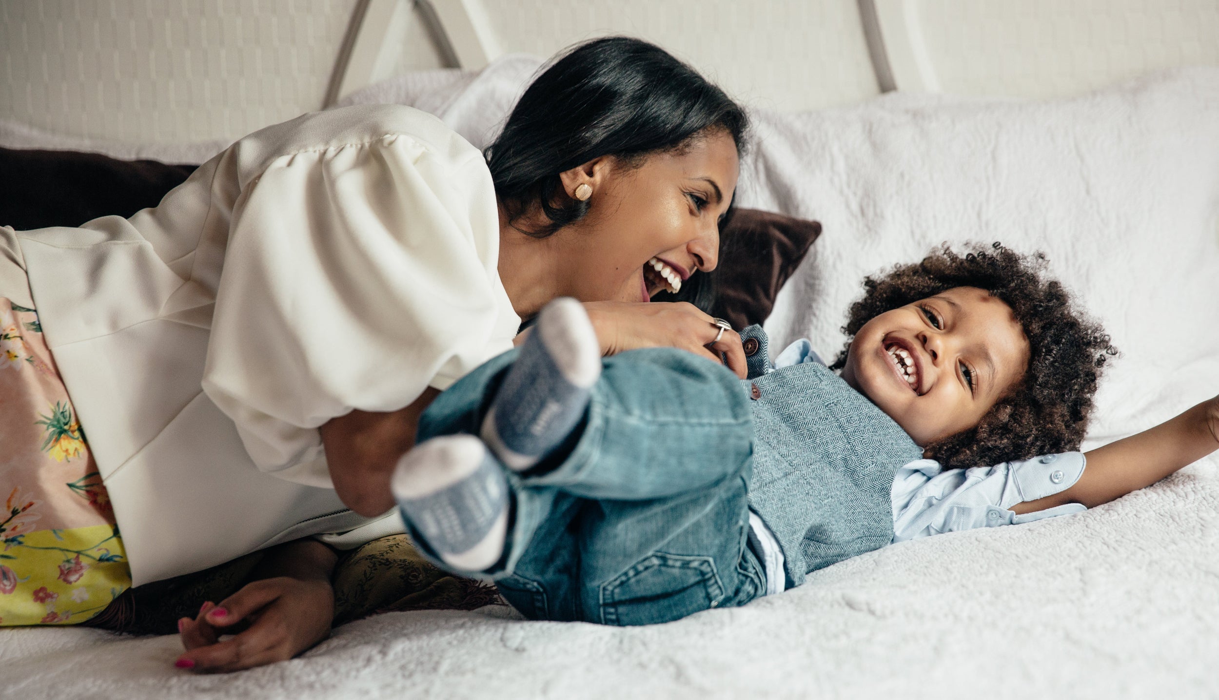 A mom tickles her son on a bed