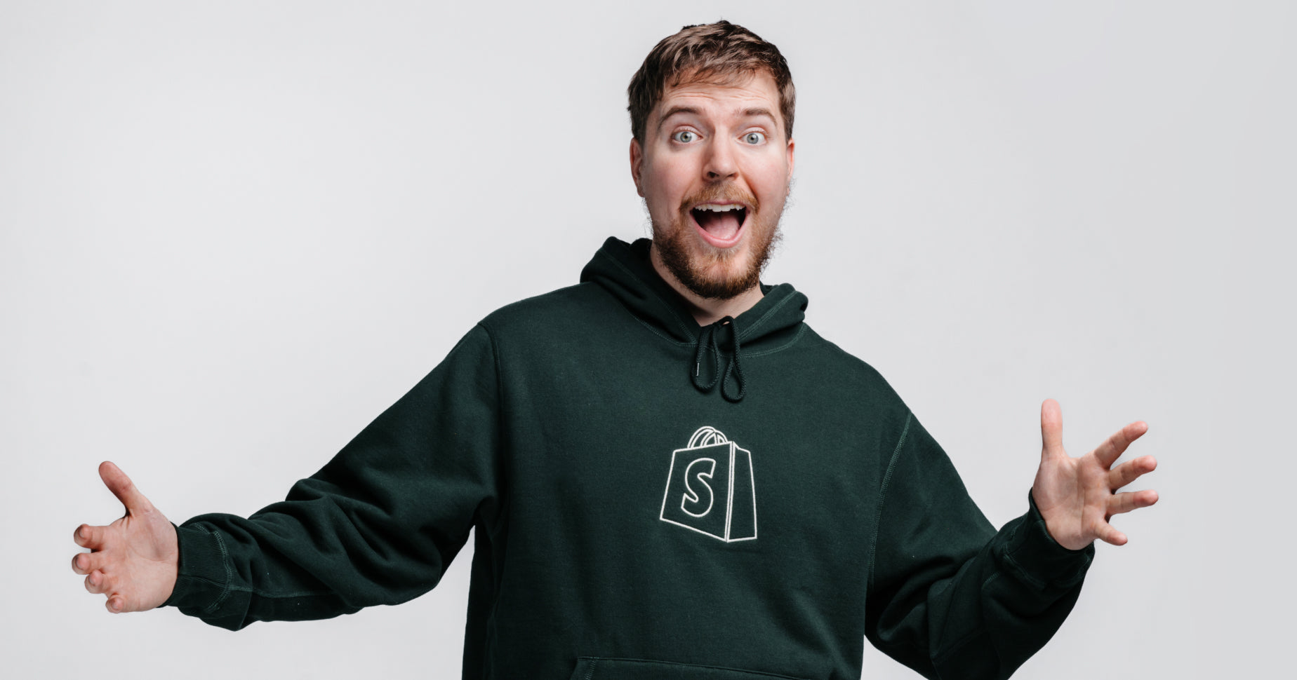 MrBeast smiling jovially with his arms open wearing a Shopify hoodie.