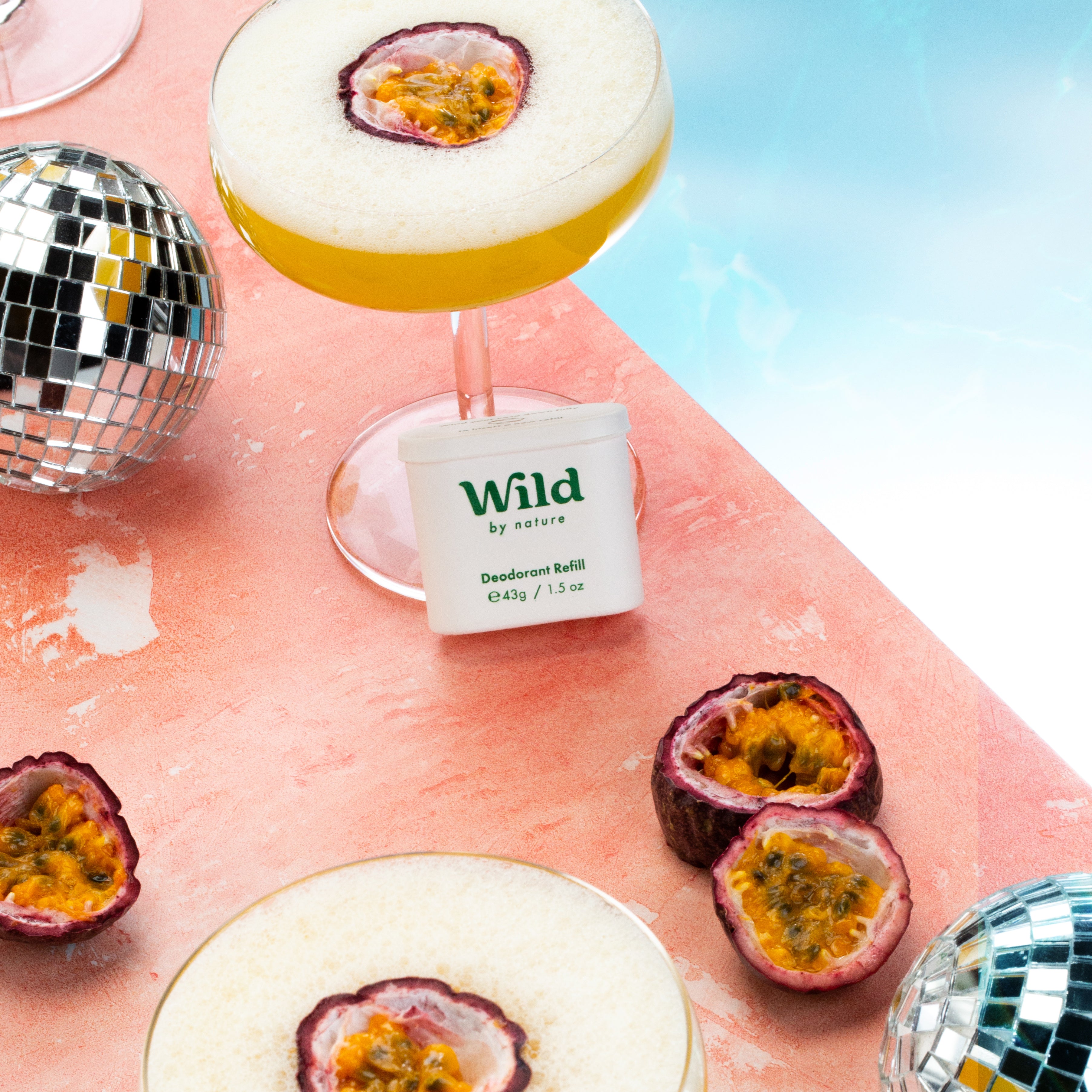 A Wild deodorant refill leans against a cocktail topped with a passion fruit surrounded by more decorative passion fruits. 