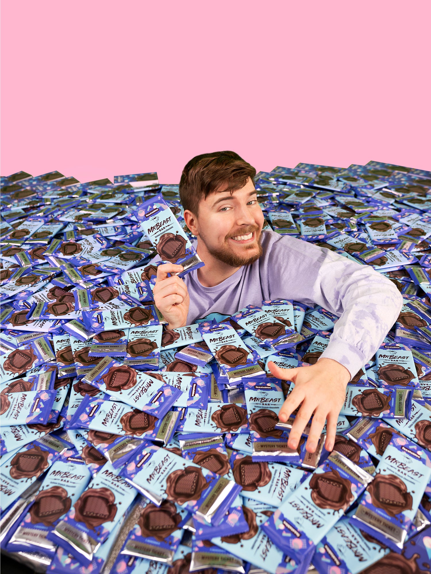 MrBeast surrounded by several Feastables chocolate bars with blue packaging. In the background is a pink backdrop.