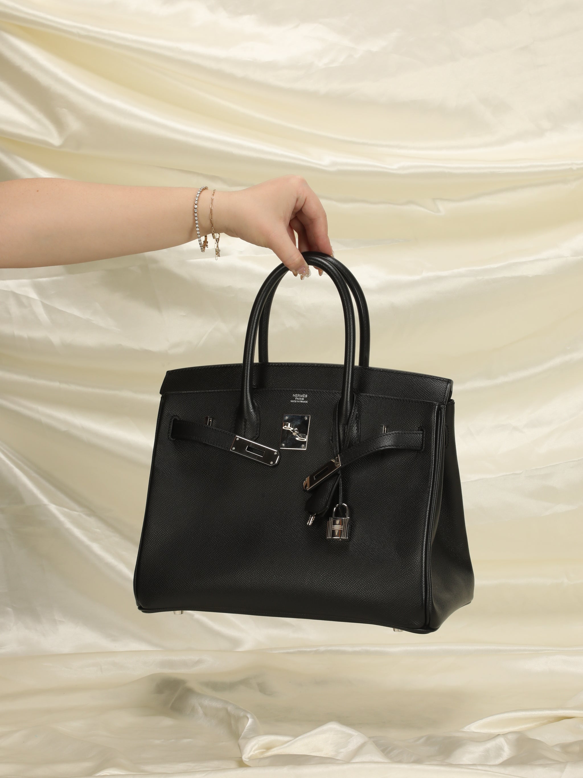 Nica’s hand holding a vintage black Hermès Birkin with silver hardware.