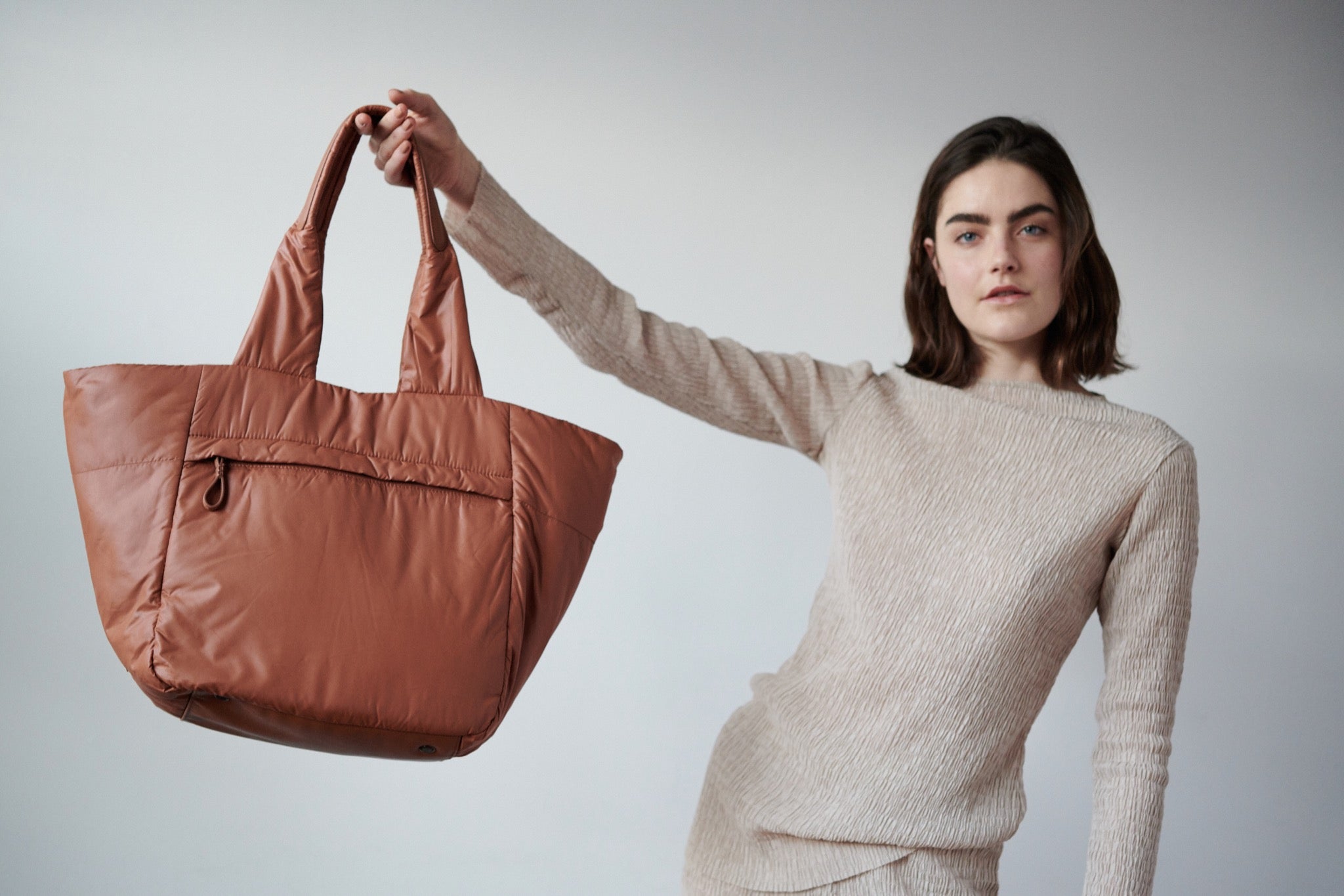 A model in a cream outfit holds a Caraa designed tote. 