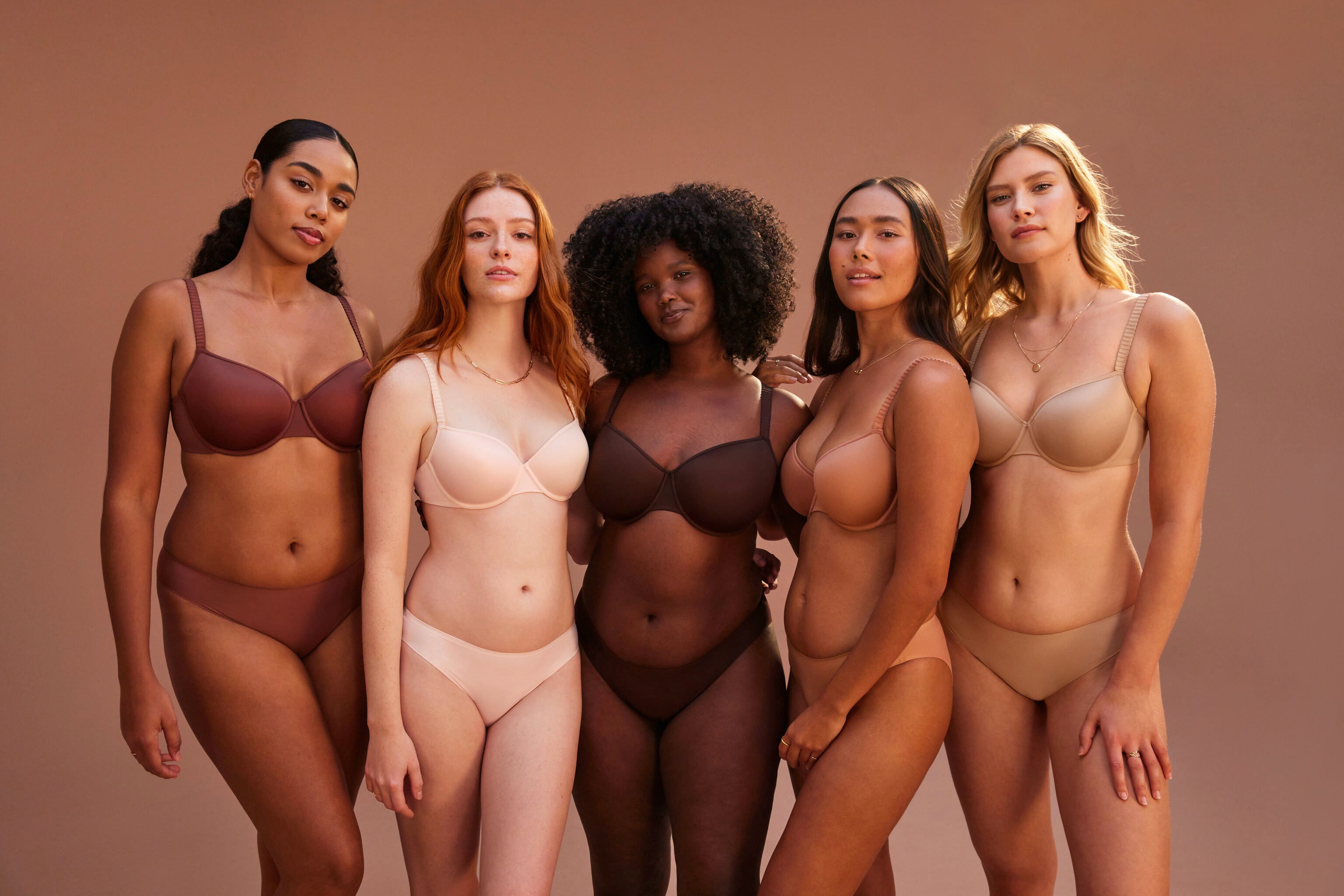 A group of five women wearing bras and underwear from ThirdLove against a brown-colored backdrop. 