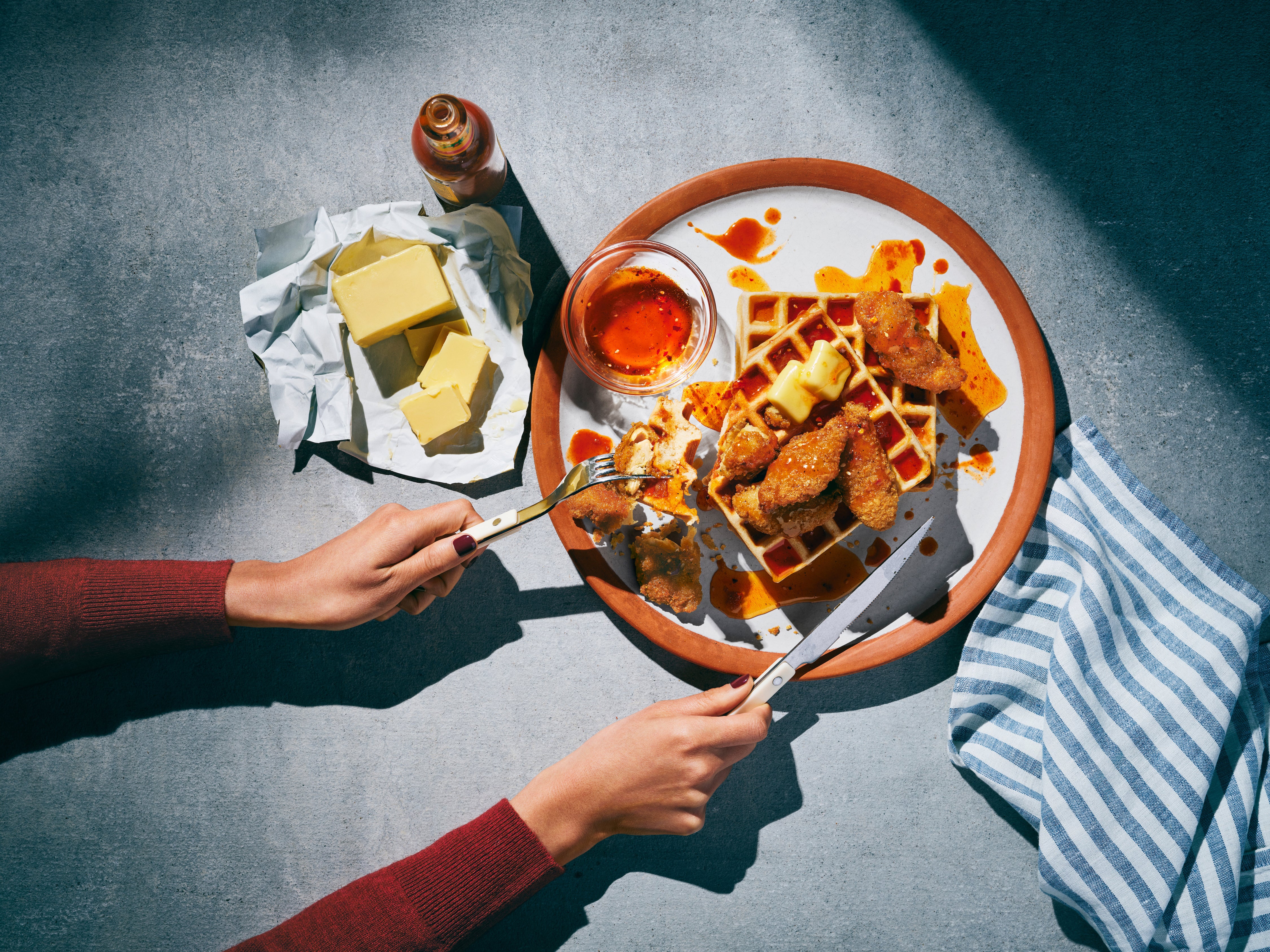 Daring breaded chicken being picked up on a fork on top of a plate of waffles.