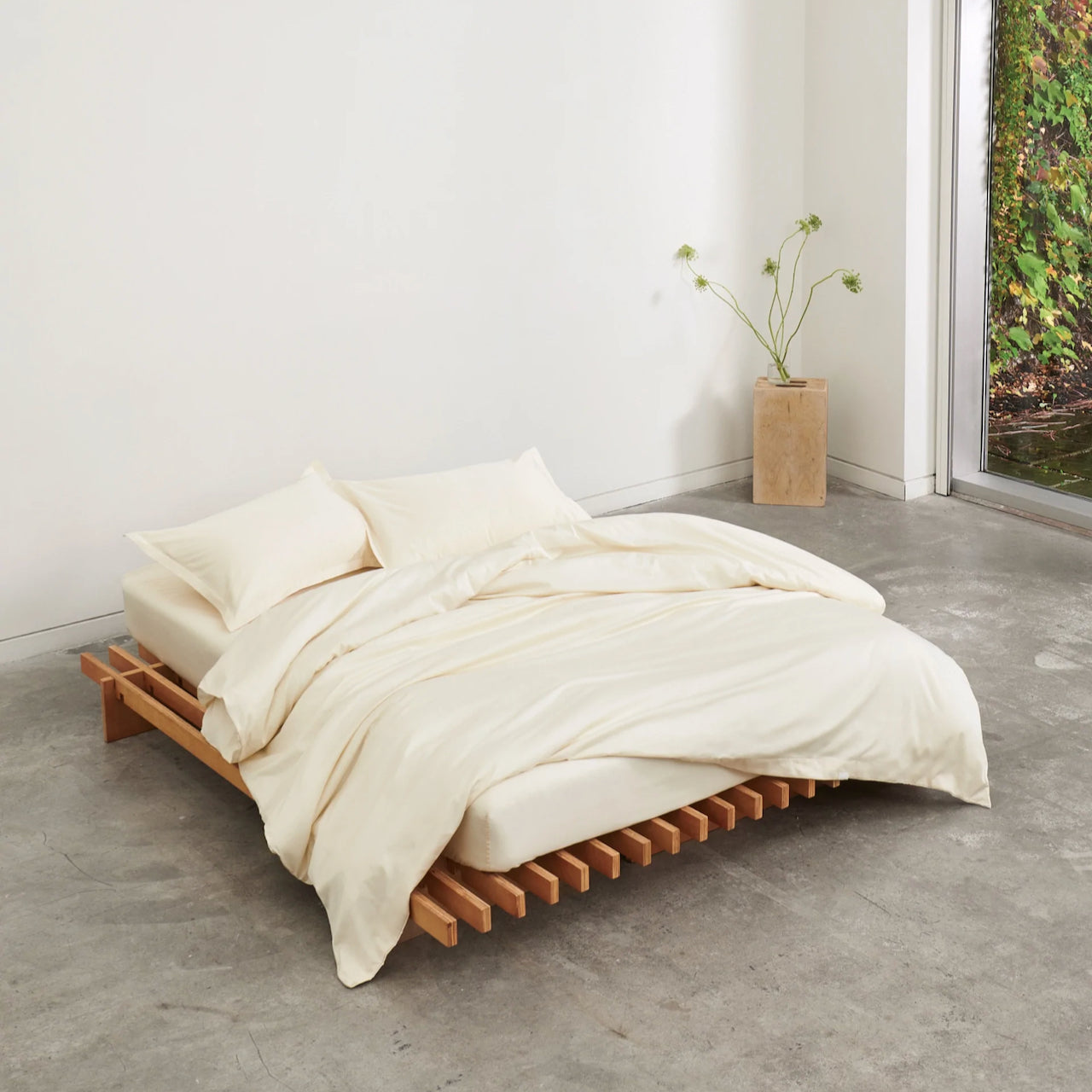 A wooden framed bed with cream cotton bedding by KOTN in a bedroom setting. 