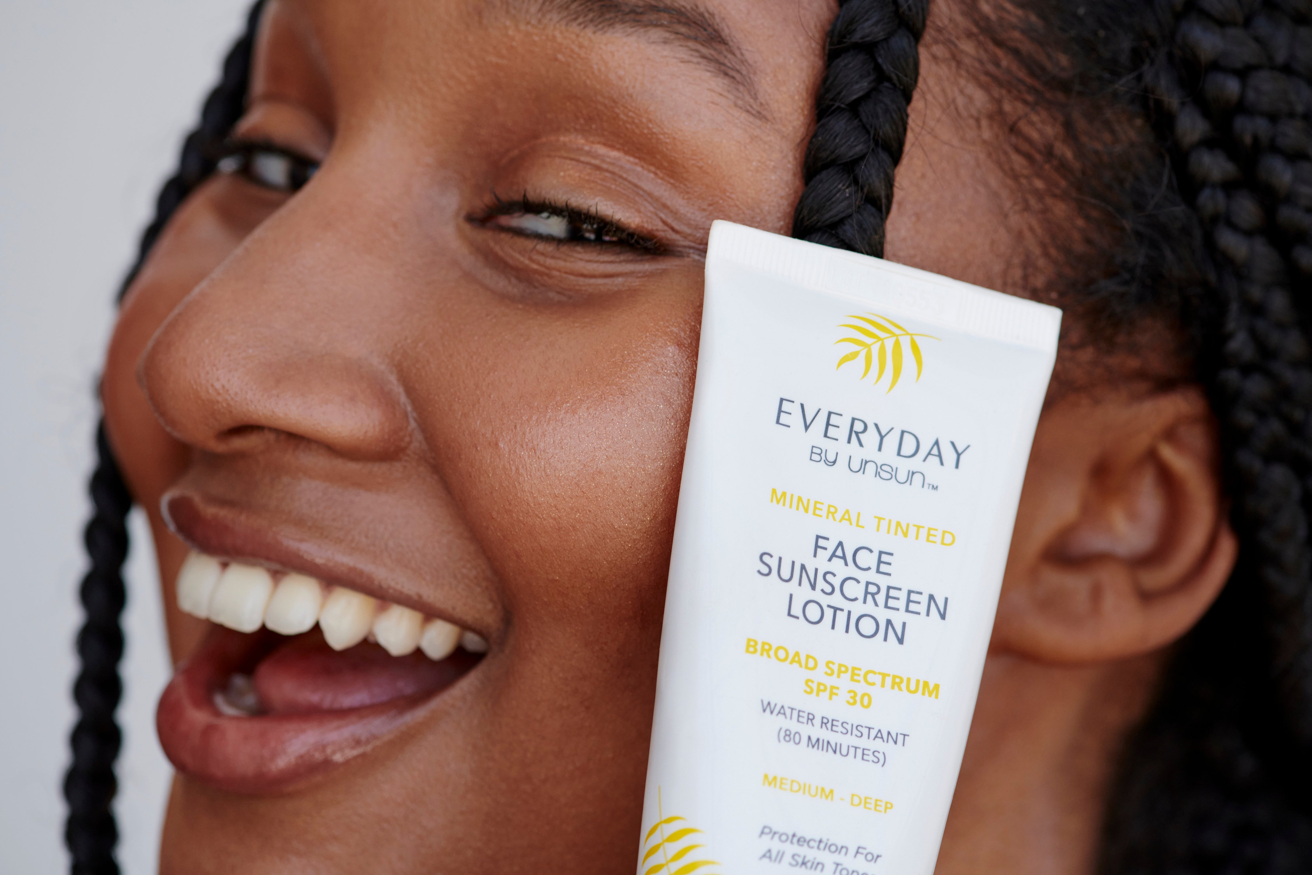 A model smiles with Unsun Cosmetics’ Everyday face sunscreen lotion up to her cheek. 