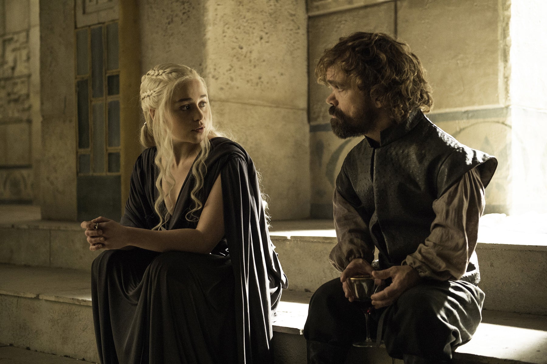 Daenerys and Tyrion Lannister sit on a step and talk to each other.