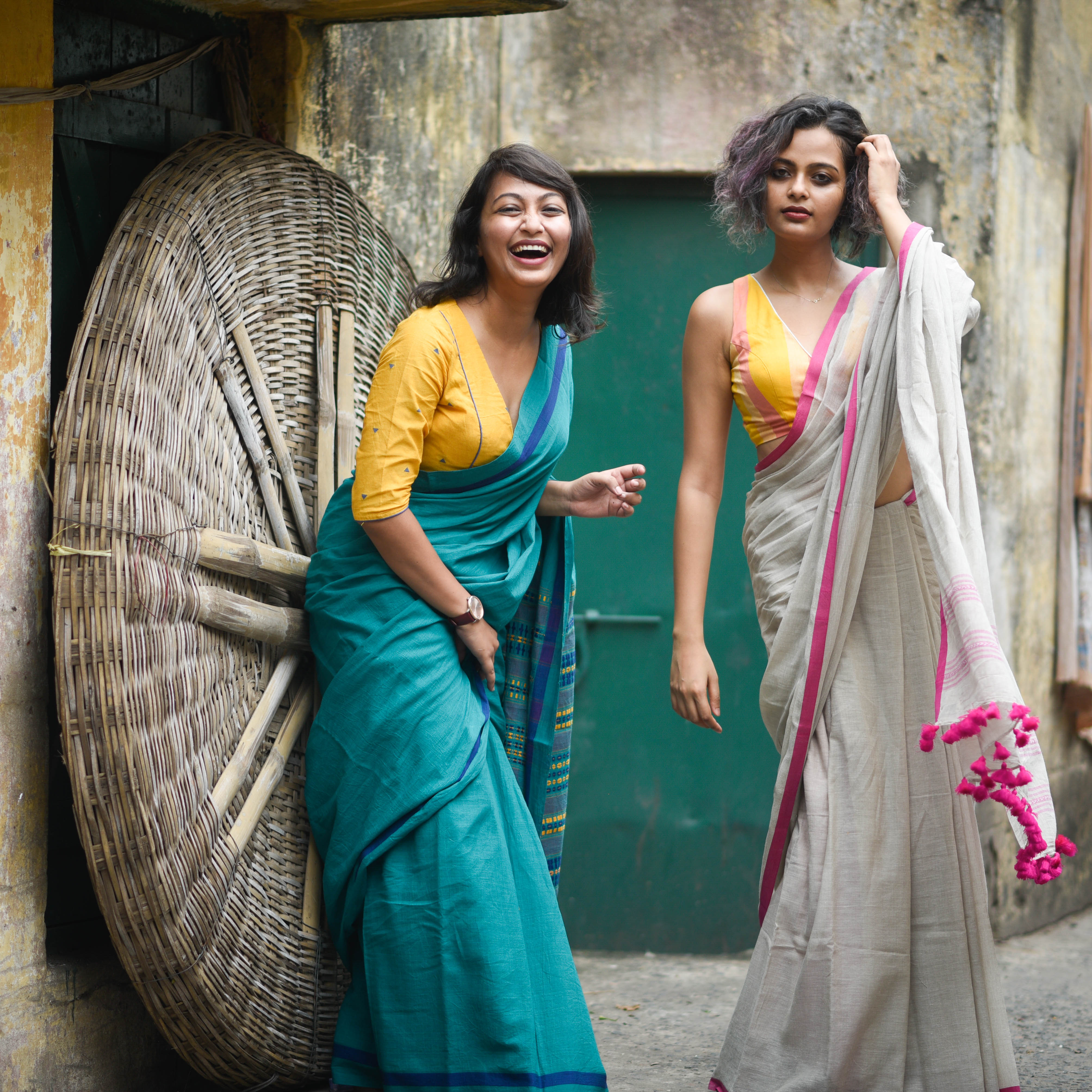 Taniya, in a blue saree with yellow blouse, stands with sister, Sujata who is in a gray saree with pink details and a yellow top. 