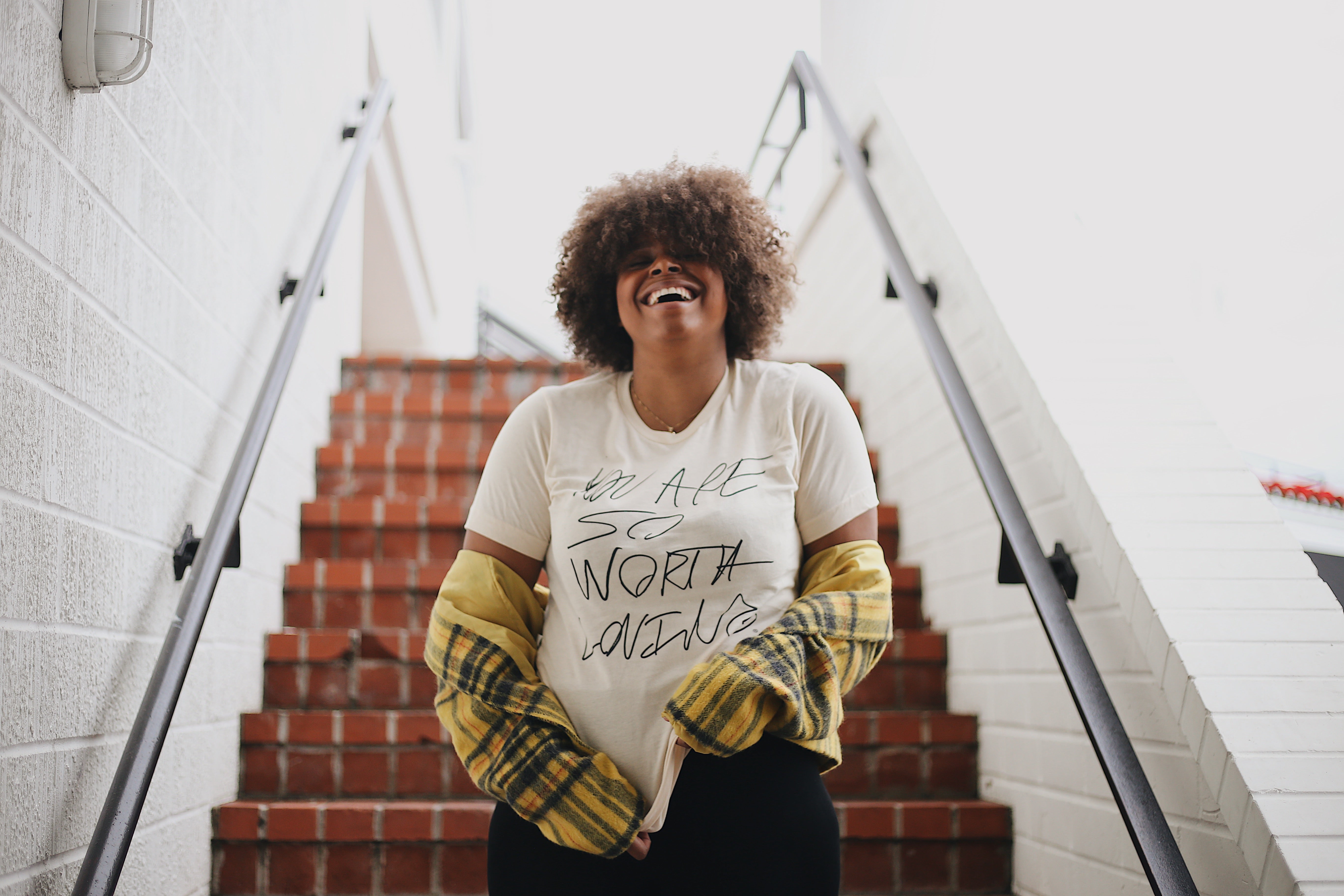 A model near a set of stairs wearing a So Worth Loving shirt. 