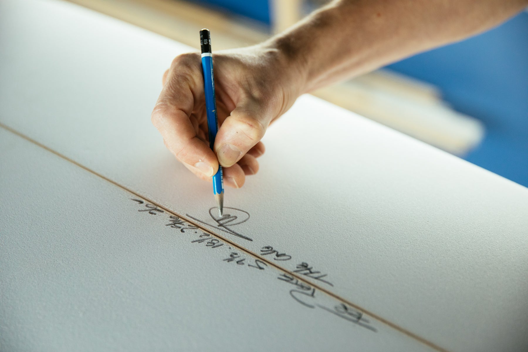 Close up of Stef Aftanas’ hand signing a surfboard with a pencil.