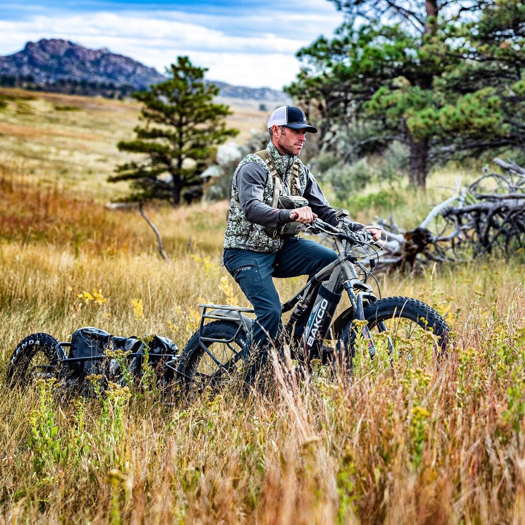 Hunter riding an e-bike with a trailer attachment through a field.