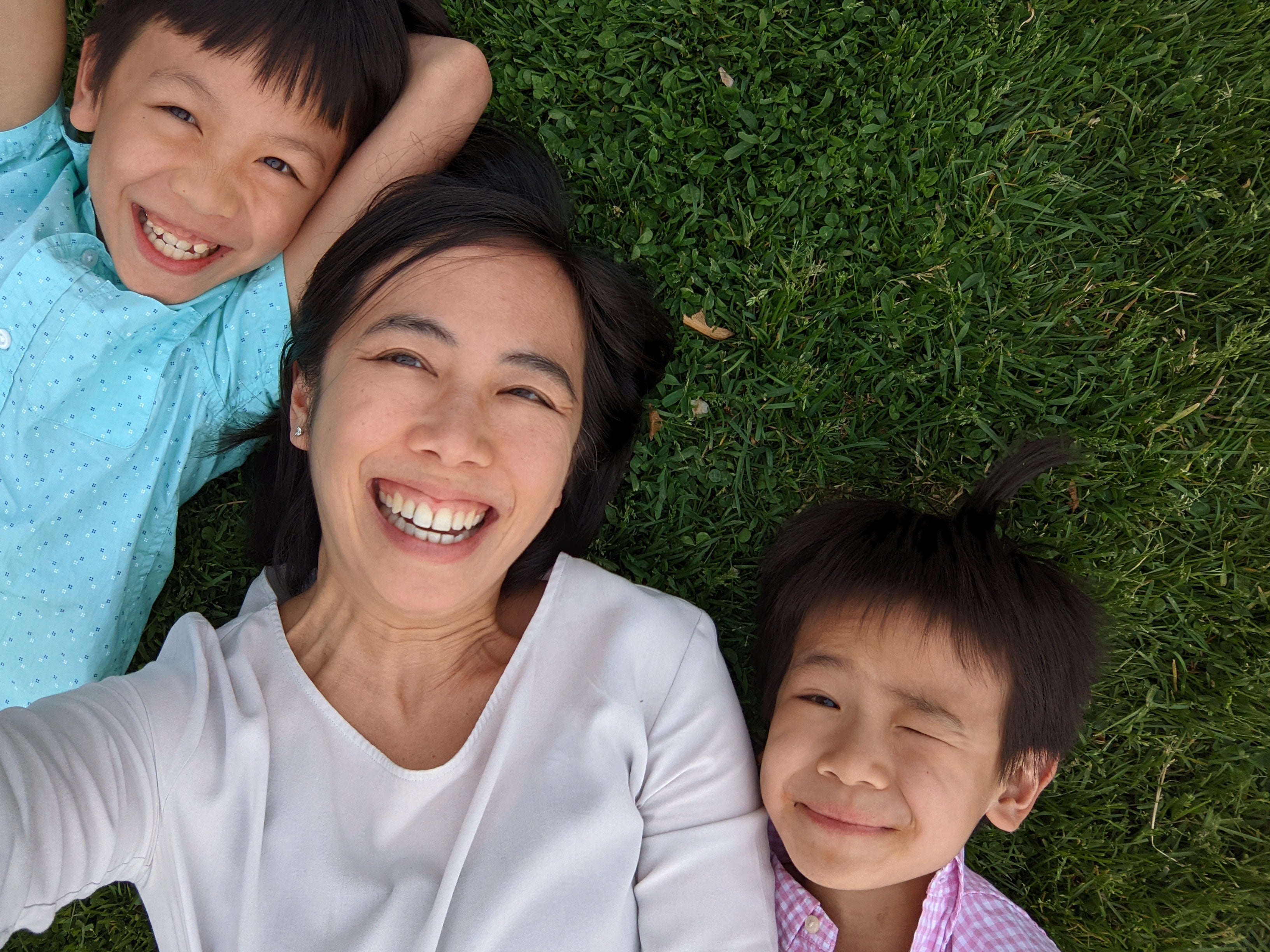 A woman lies in the grass laughing with her two young children