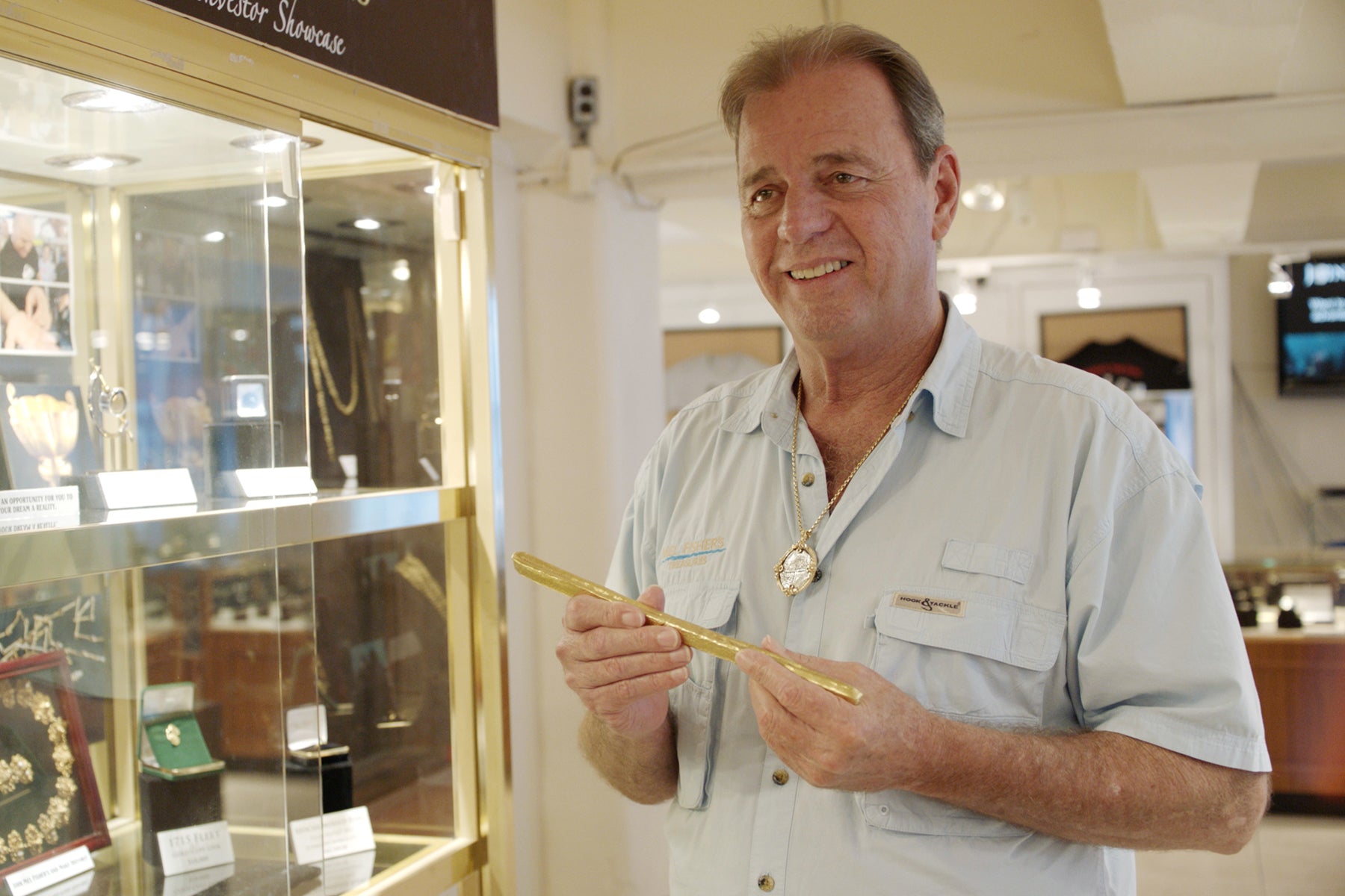 Kim Fisher, who operates Mel Fisher's Treasures in Key West, Florida holding a gold object next to a glass display cabinet filled with jewelry.