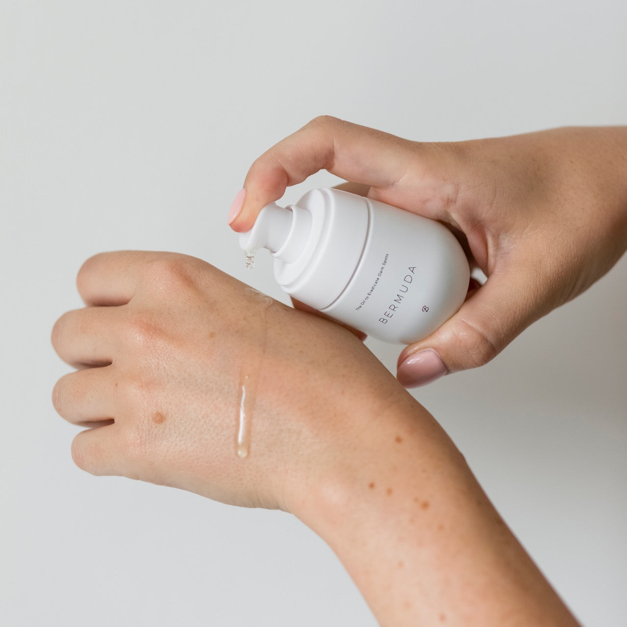 A bottle of Bermuda oil by Bushbalm held by a hand model as they apply it onto the back of their hands.