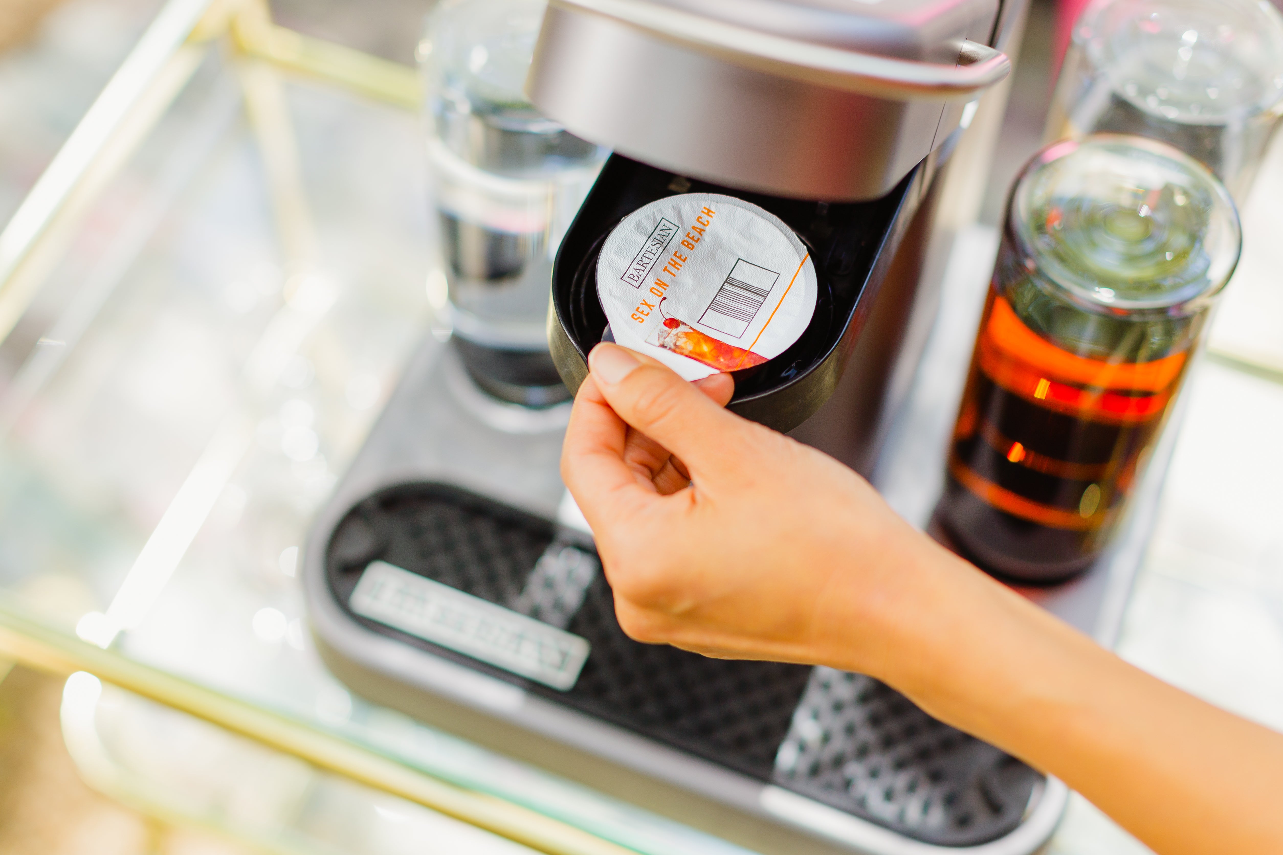 A model’s hand places a Bartesian Sex On The Beach drink capsule into the machine.