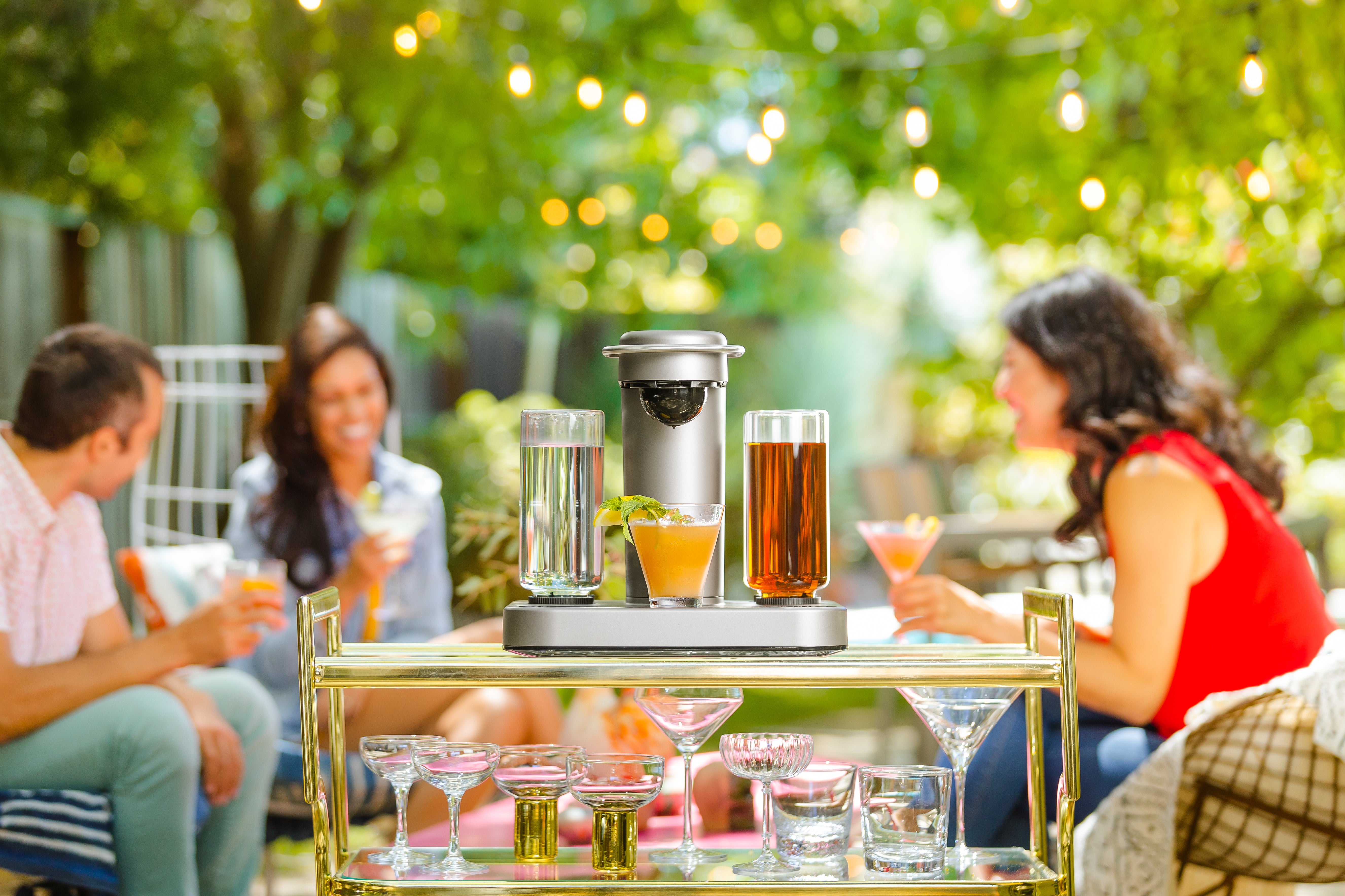The Bartesian sitting on top of a glass table with gold accents as three models enjoy their beverages in the background.