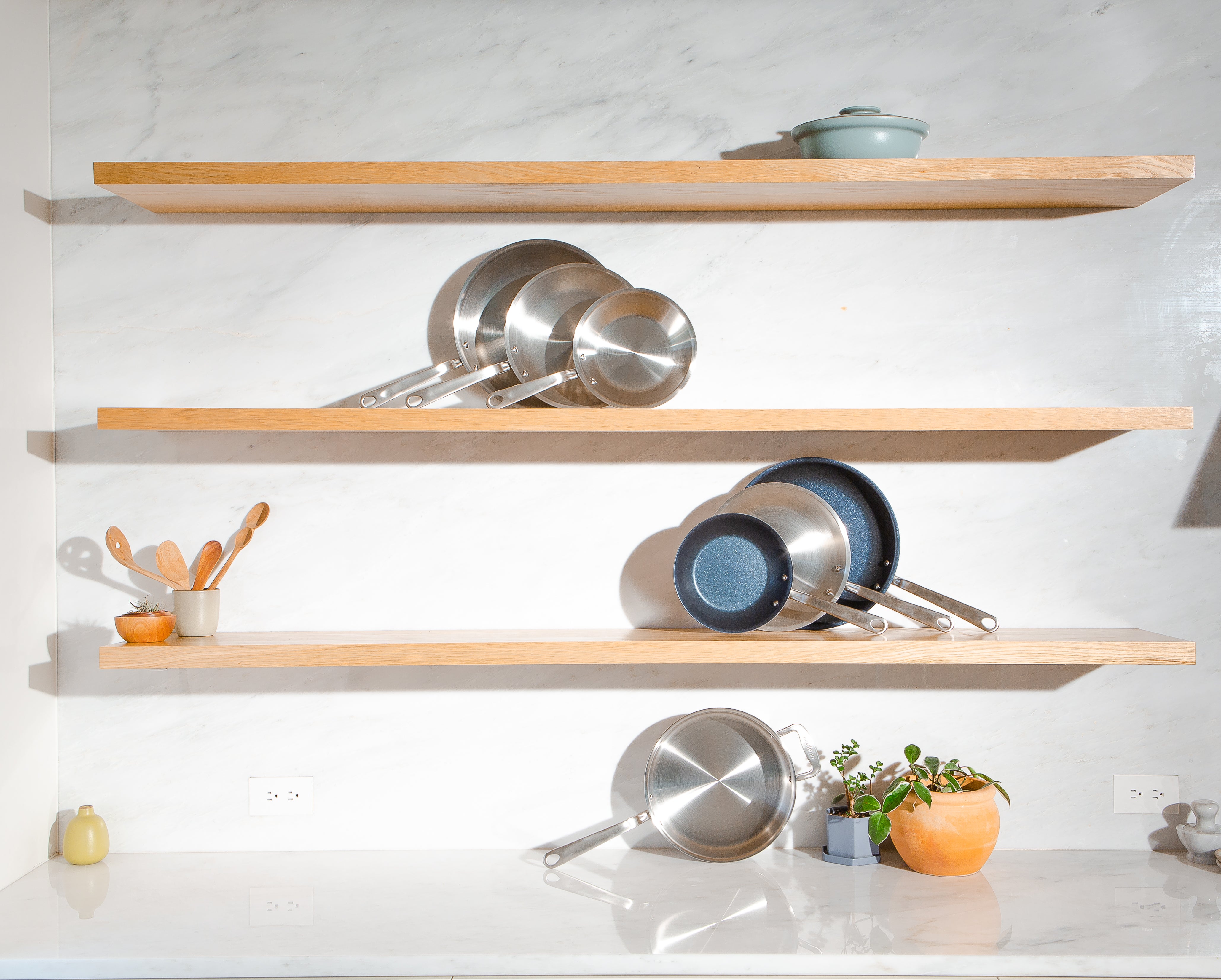 Collection of pans from Made In displayed on wooden shelves. 