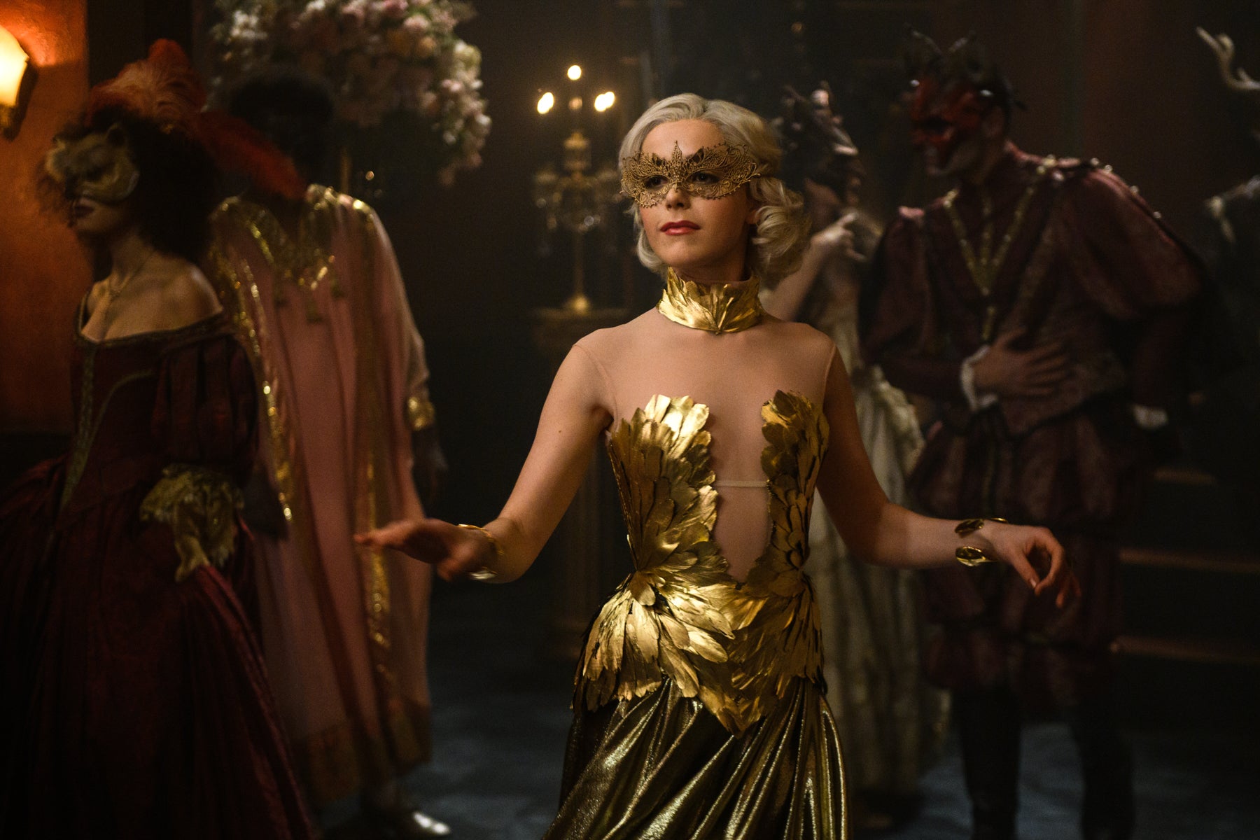 Sabrina Spellman dances in a gold dress and mask in a scene from Chilling Adventures of Sabrina.