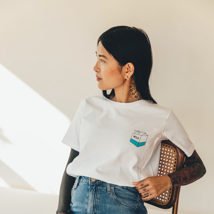 A model with tattoos wearing a white Tajinebanane T-shirt with a milk carton design.